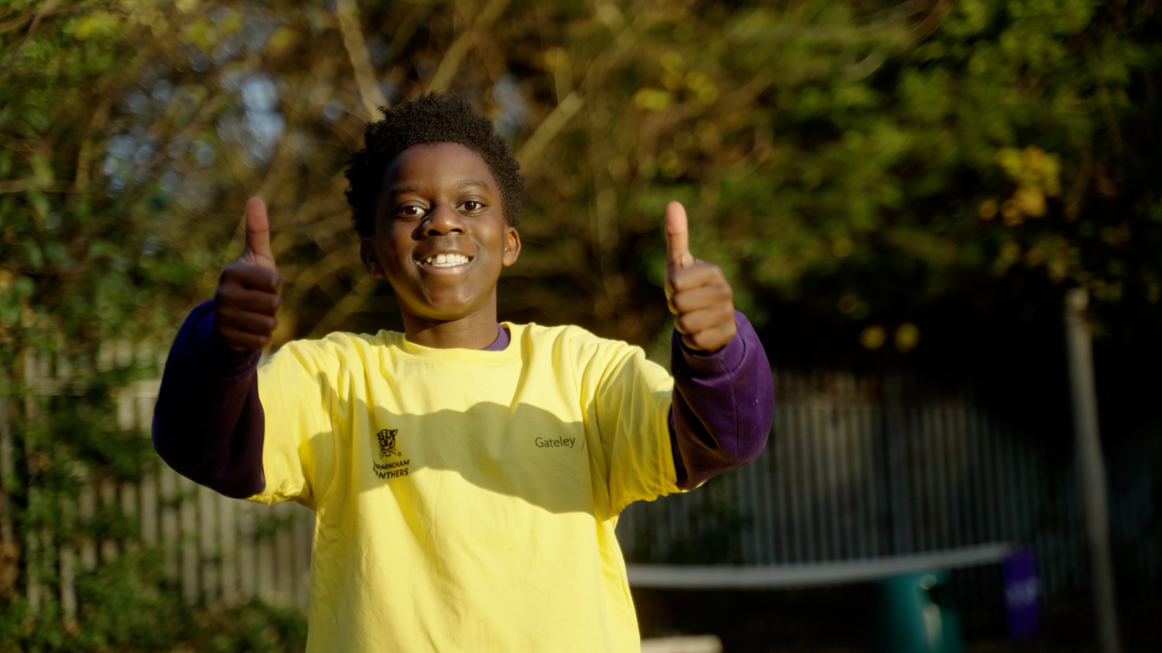 One of the children smiles to camera with both thumbs up